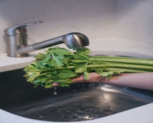 Fresh green vegetables being washed under a kitchen tap